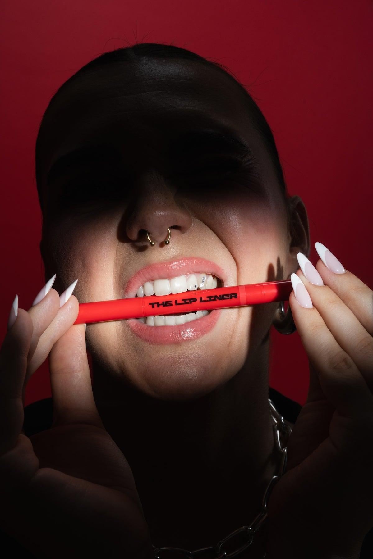 Frau hat The Lip Liner zwischen den Zähnen vor rotem Hintergrund.